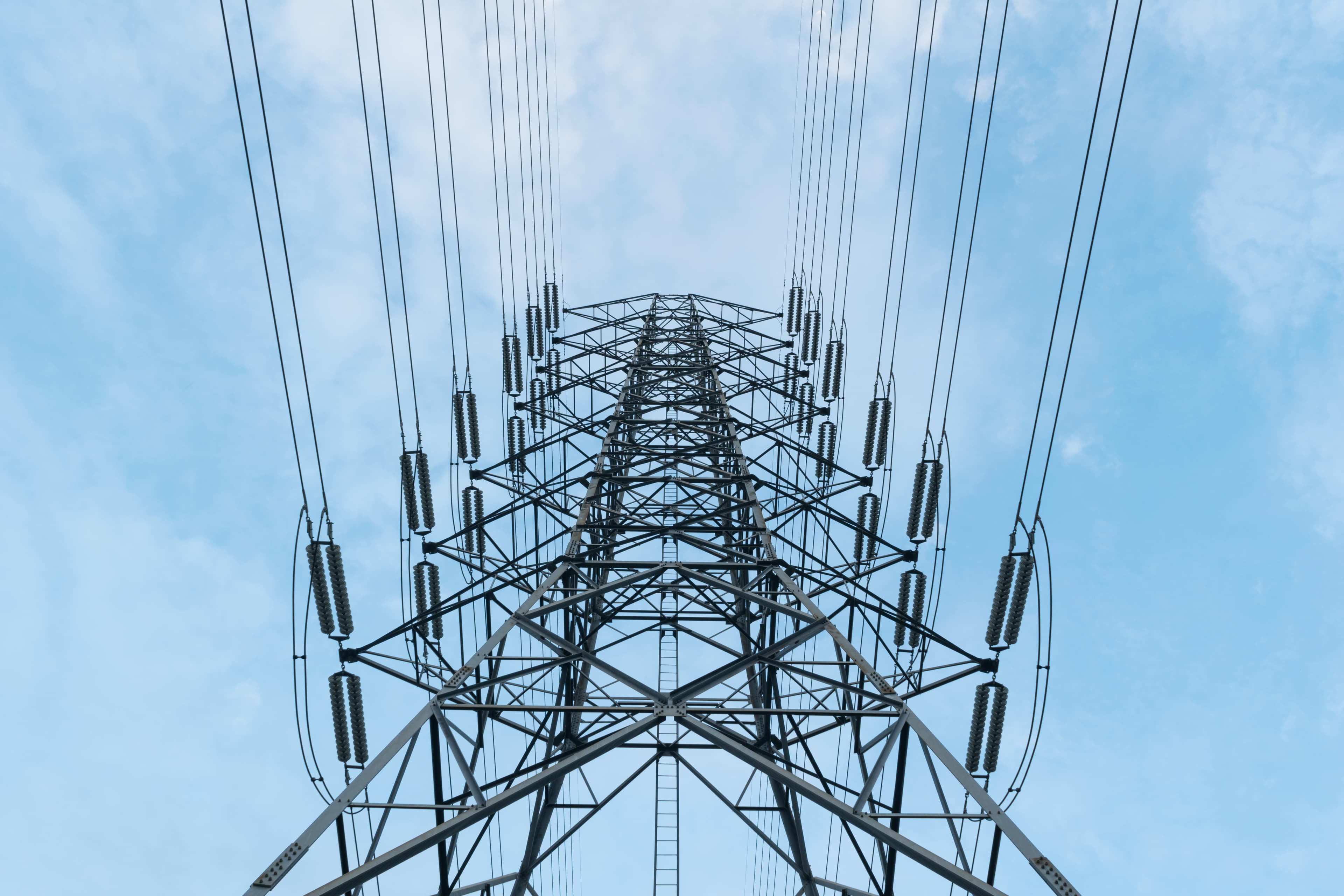 A high-voltage transmission pylon against a clear blue sky.